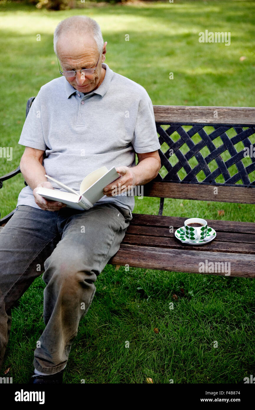 Un vecchio uomo che legge un libro in un parco. Foto Stock