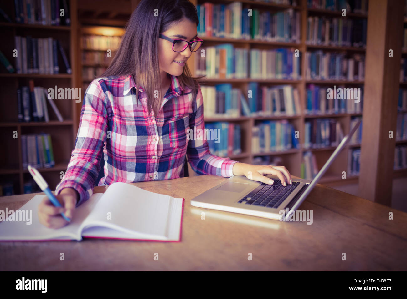 Studentessa con libro utilizzando laptop Foto Stock