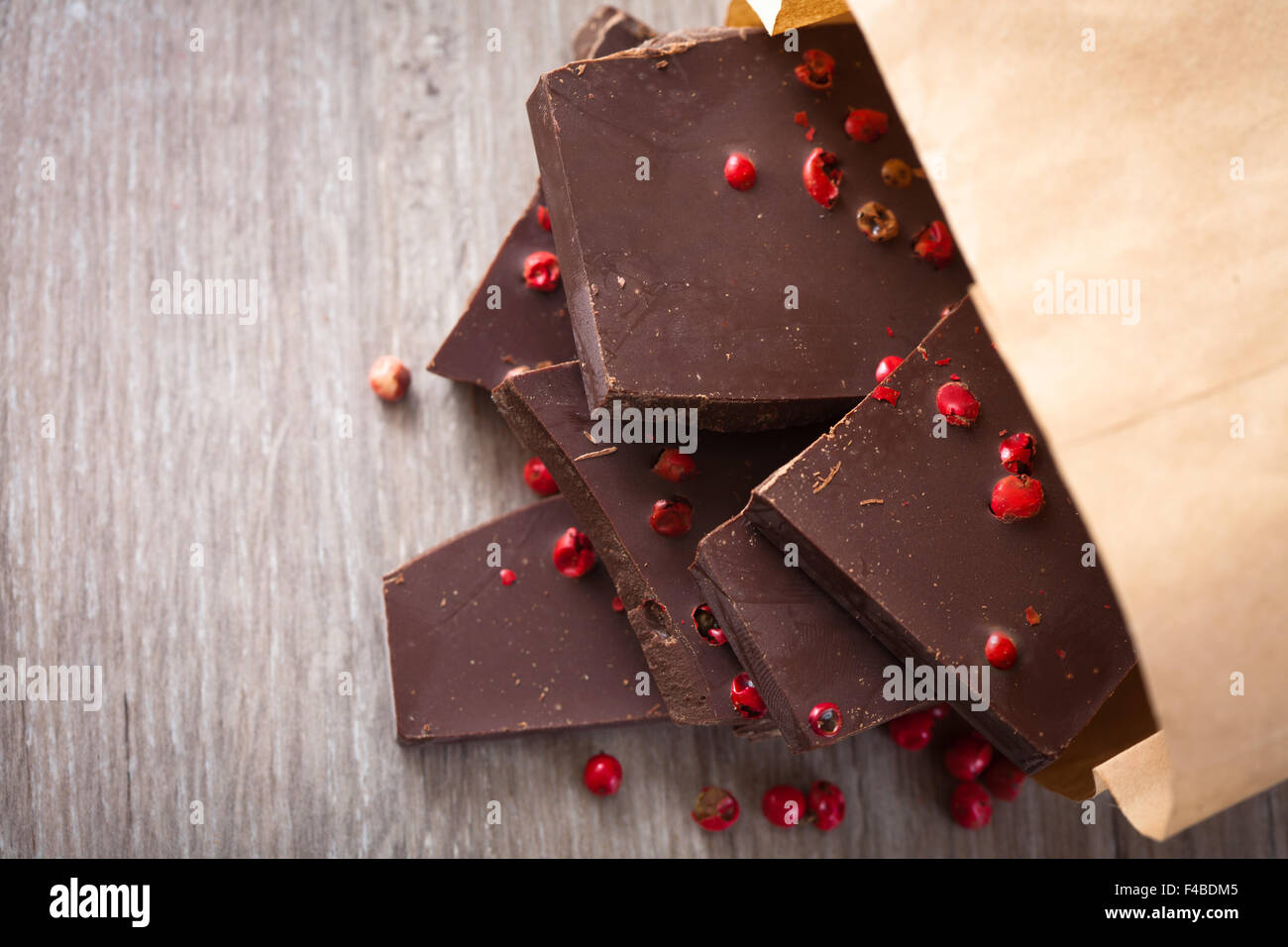 Pezzi di cioccolato fondente con pepe rosa sul tavolo Foto Stock