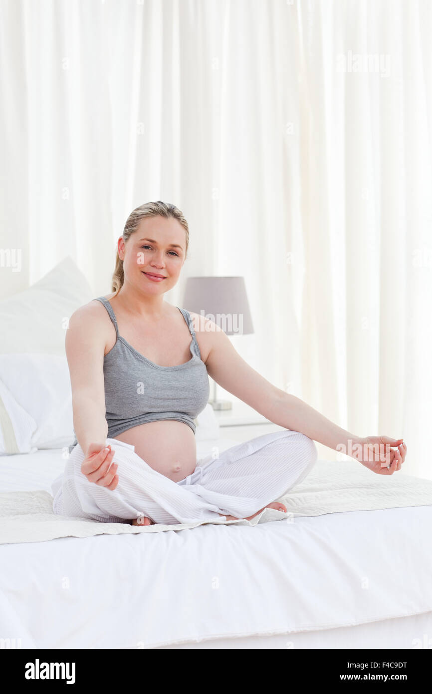 Donna incinta a praticare yoga sul suo letto Foto Stock