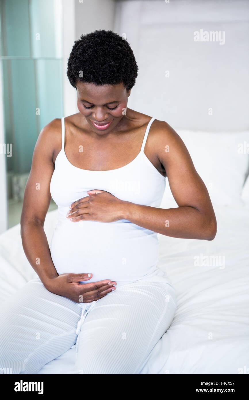 Sorridente donna incinta seduta sul suo letto Foto Stock