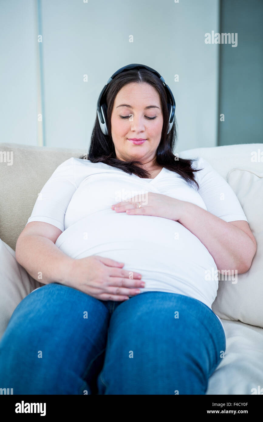 Donna incinta con cuffie di toccare la sua pancia Foto Stock