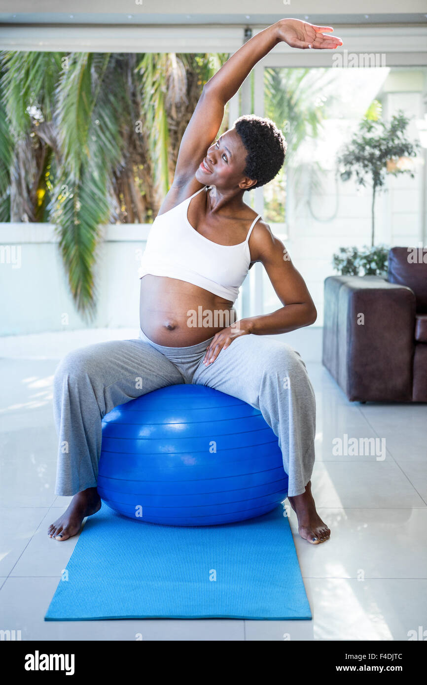 Allegra donna incinta stretching seduti sulla palla ginnica Foto Stock