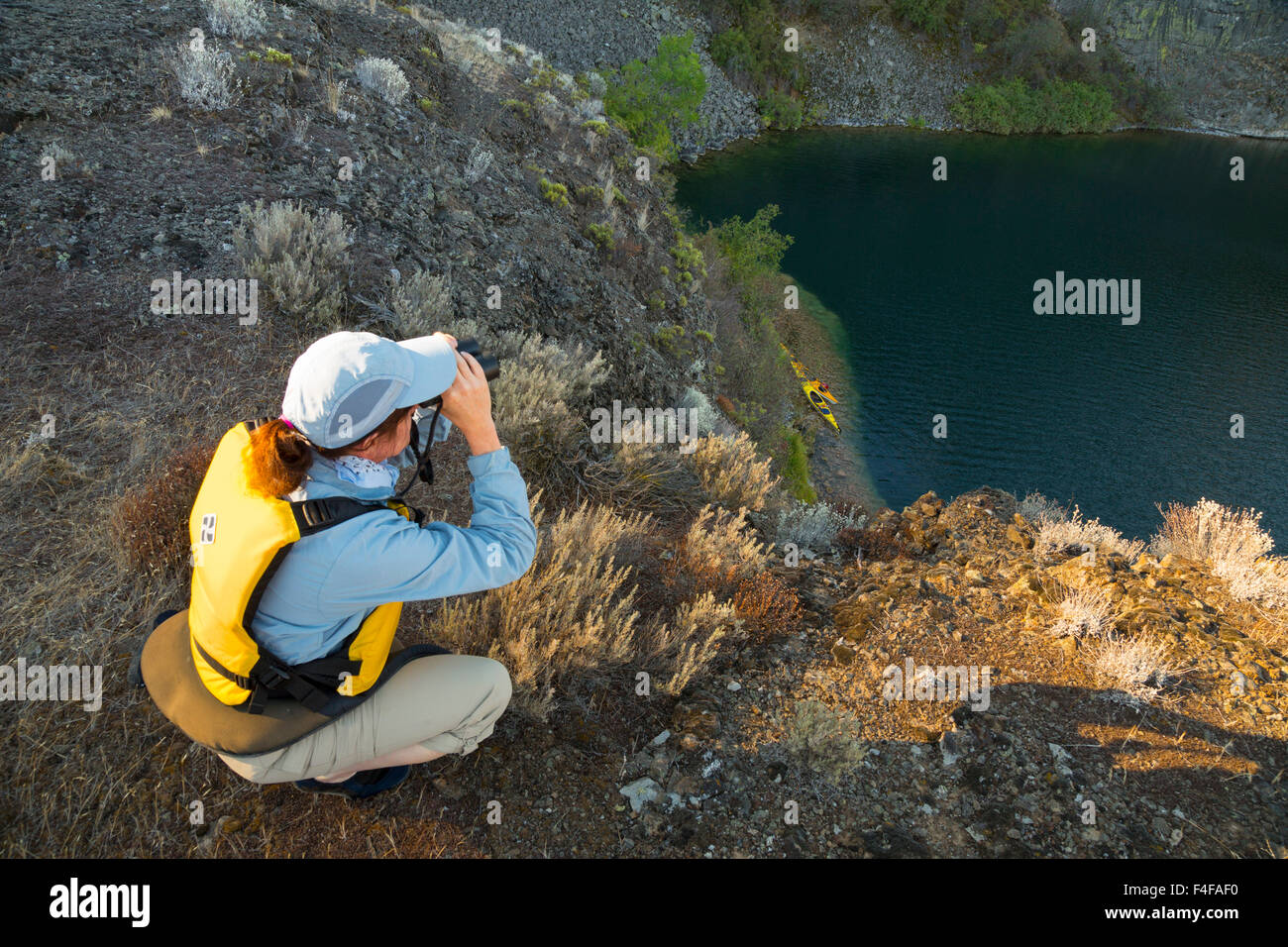 Stati Uniti d'America, nello Stato di Washington. Donna kayaker di mare a terra con il binocolo su un profondo lago vicino cade a secco, Grand Coulee, parte dell'alluvione di Missoula incanalato scablands (MR). Foto Stock