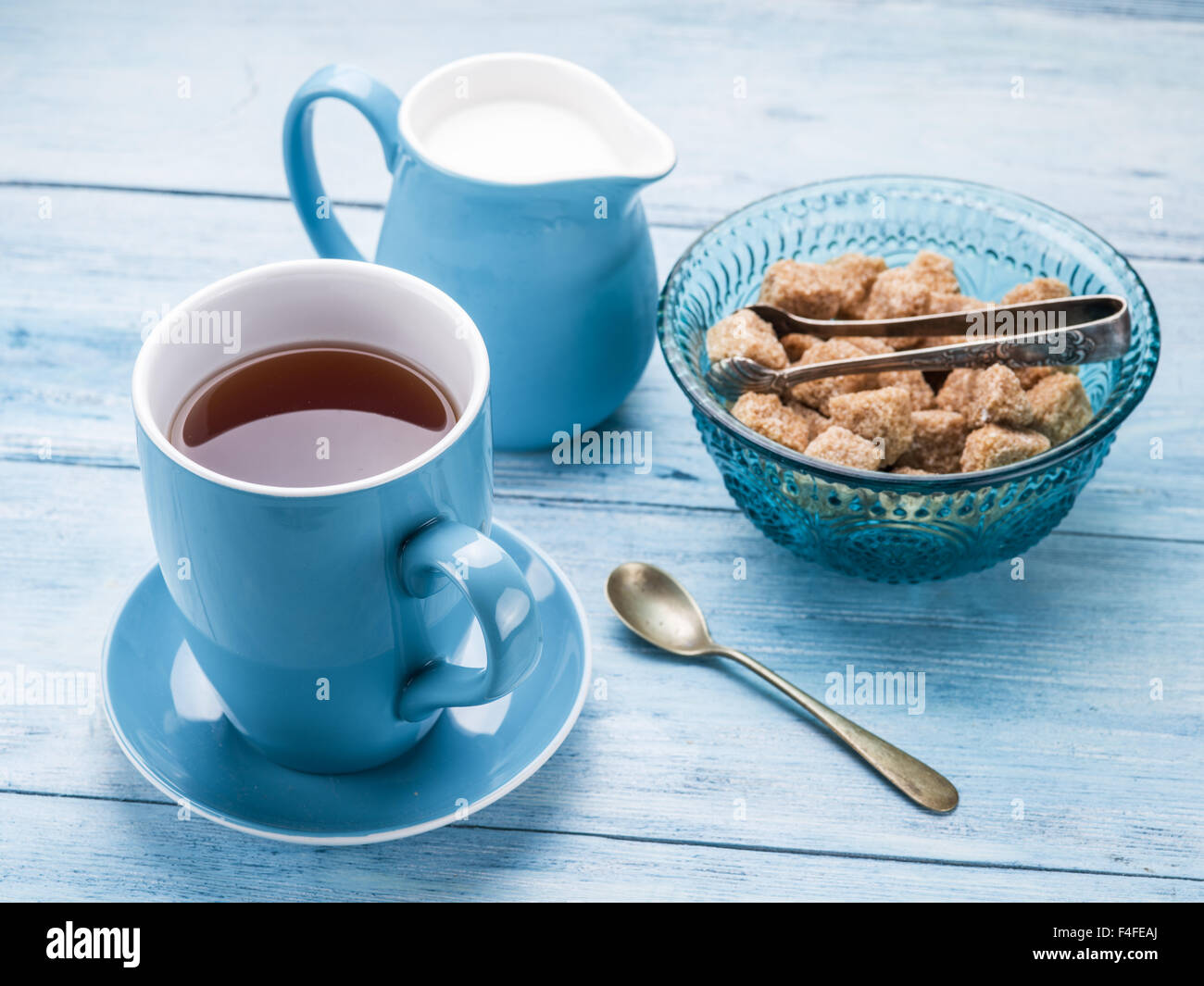 Tazza di tè, il bricco per il latte e lo zucchero di canna i cubi su vecchio blu tavolo in legno. Foto Stock