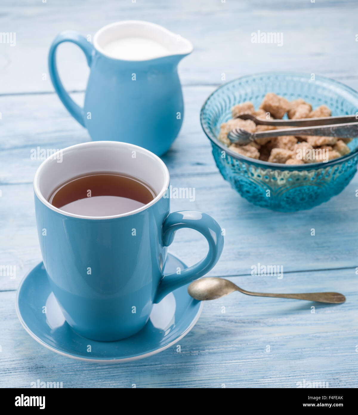 Tazza di tè, il bricco per il latte e lo zucchero di canna i cubi su vecchio blu tavolo in legno. Foto Stock