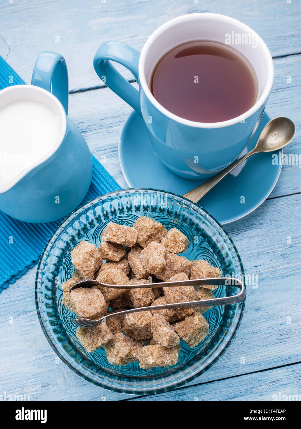 Tazza di tè, il bricco per il latte e lo zucchero di canna i cubi su vecchio blu tavolo in legno. Foto Stock