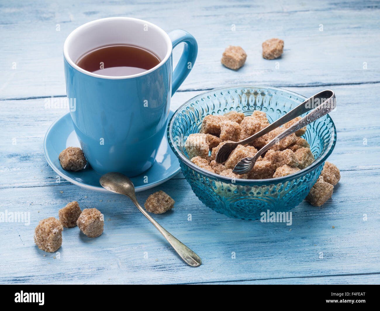 Tazza di tè e zucchero di canna i cubi su vecchio blu tavolo in legno. Foto Stock