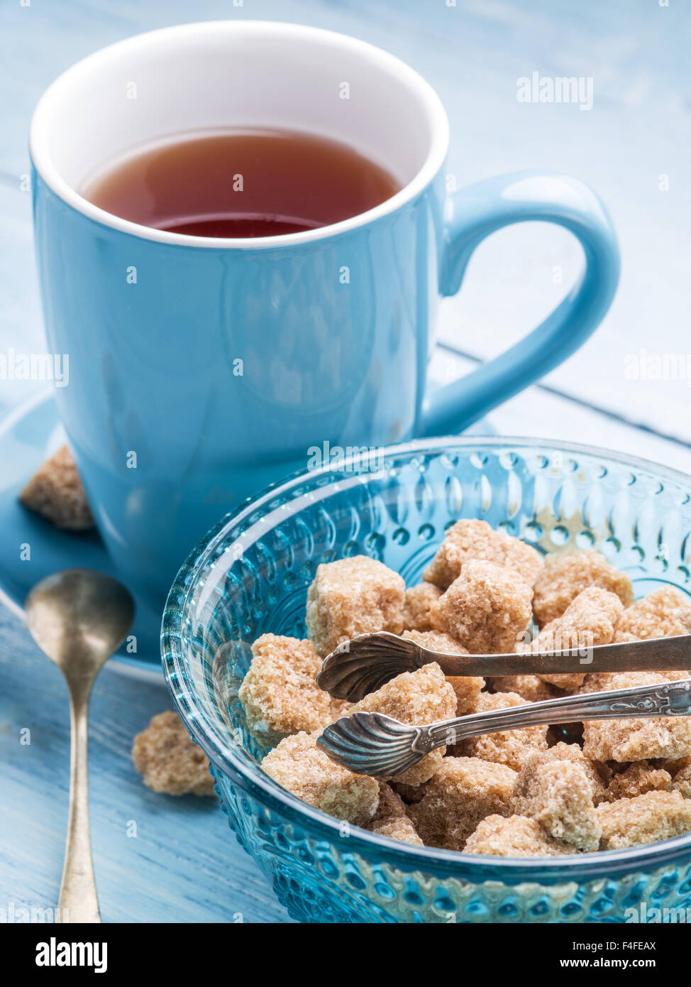Tazza di tè e zucchero di canna i cubi su vecchio blu tavolo in legno. Foto Stock