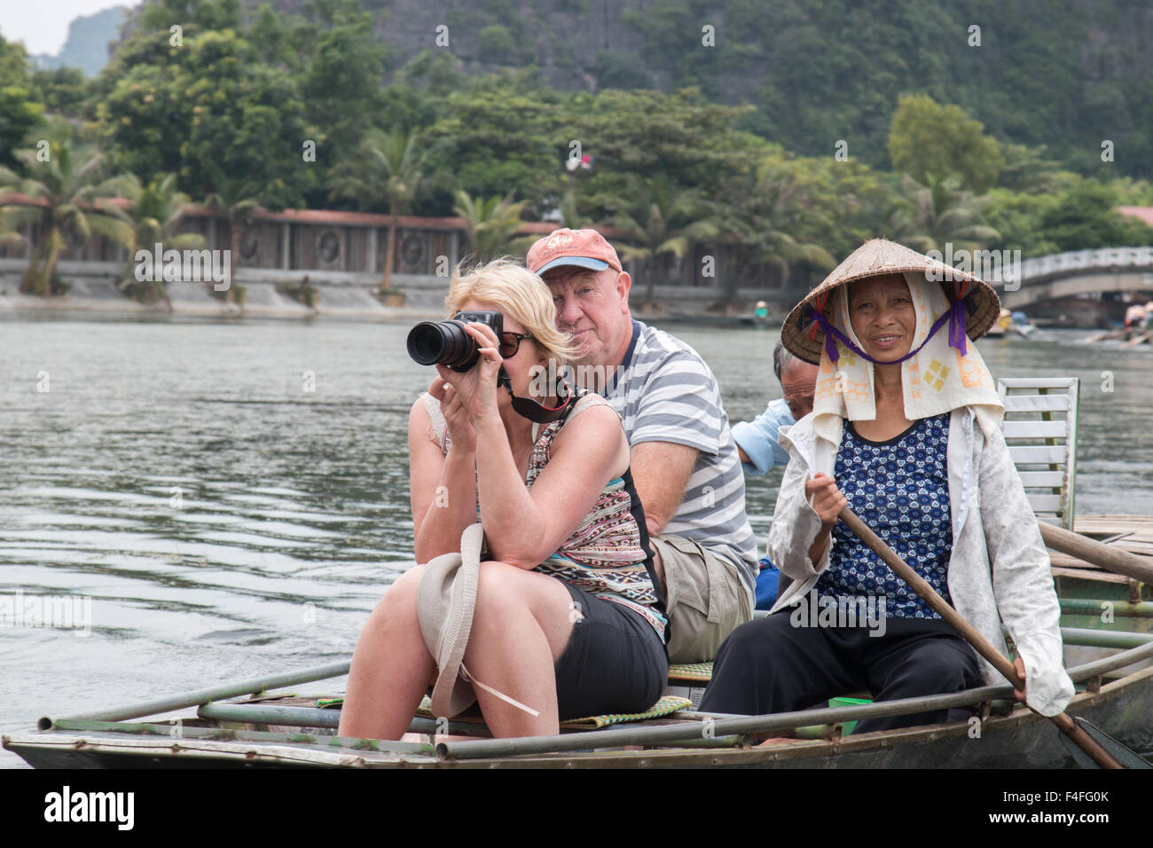 Il vietnamita l uomo e la donna le barche a remi con due turisti occidentali lungo ngo dong fiume,Tam Coc,Ninh Binh,Vietnam Foto Stock