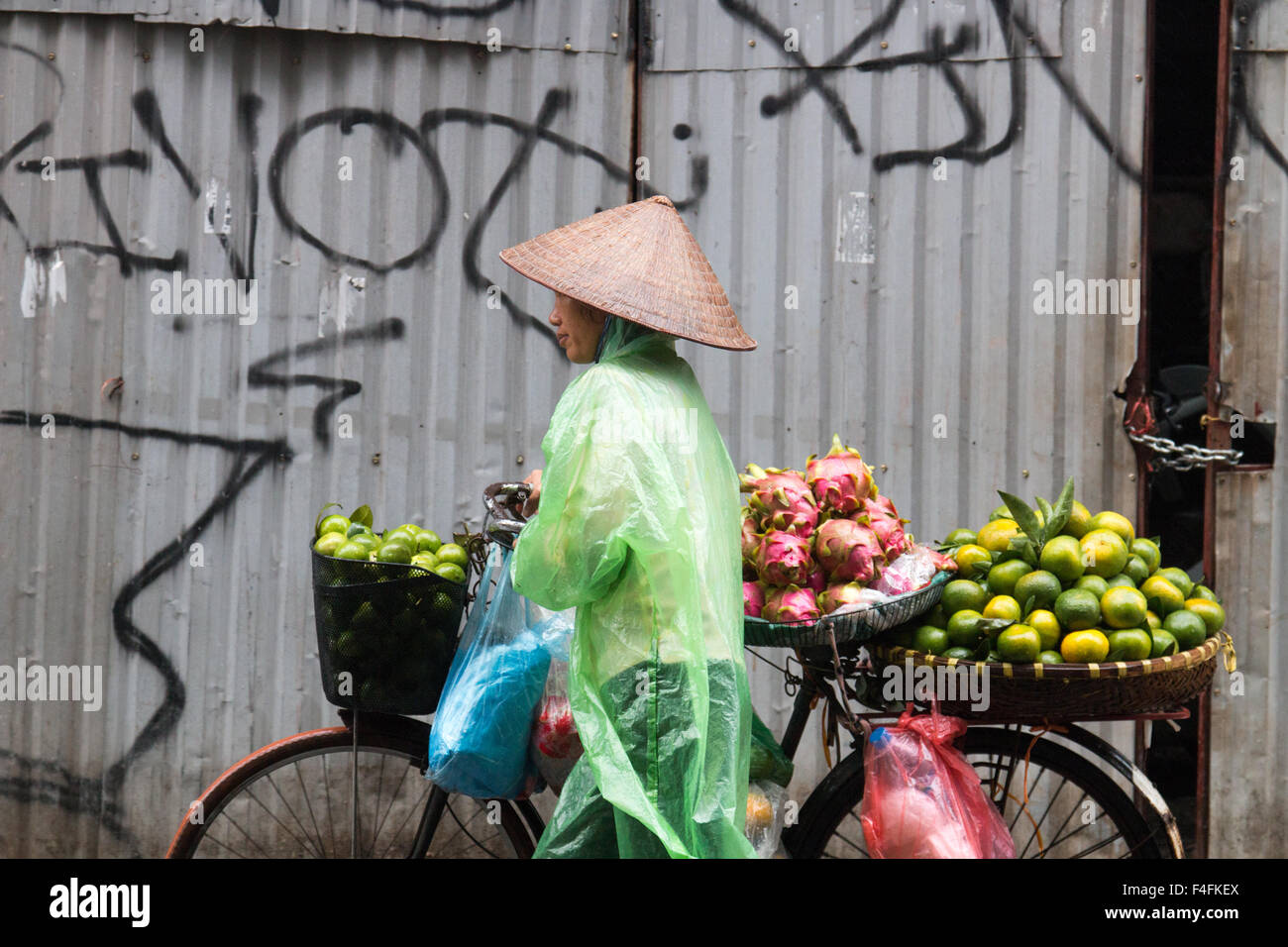 Signora vietnamita per la vendita di frutta da lei in bicicletta in Hanoi old quarter, indossando il mac in plastica per tenere a secco da tempeste,Vietnam Foto Stock