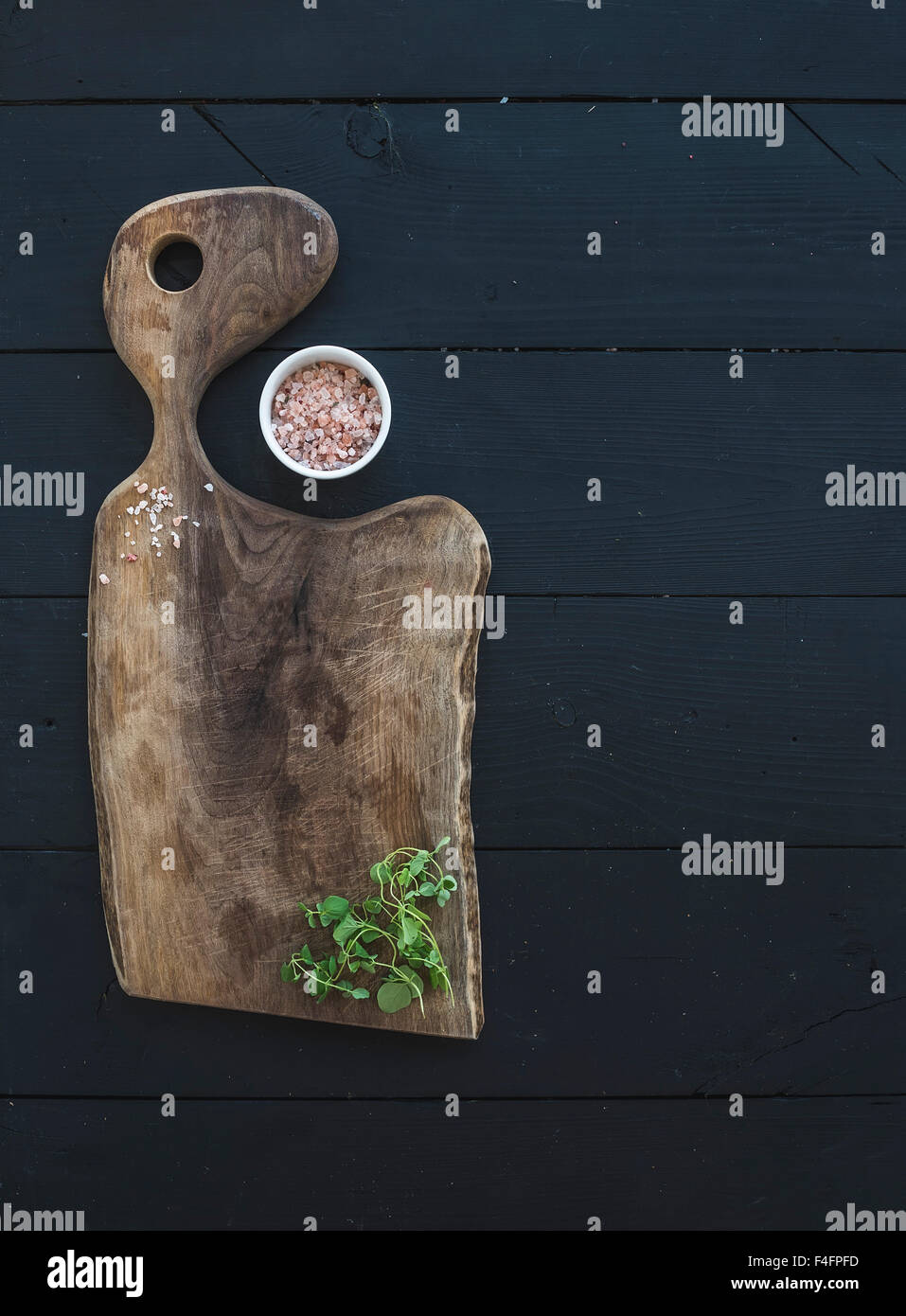 Cucina-ware set. Vecchio rustico tagliere realizzato in legno di noce, sale e origano herb su uno sfondo nero, vista dall'alto, copia spa Foto Stock