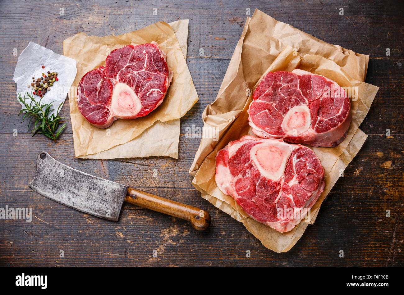 Crudo fresco di taglio trasversale di Stinco di vitello e condimenti per la produzione di Osso Buco su sfondo di legno con carne cleaver Foto Stock
