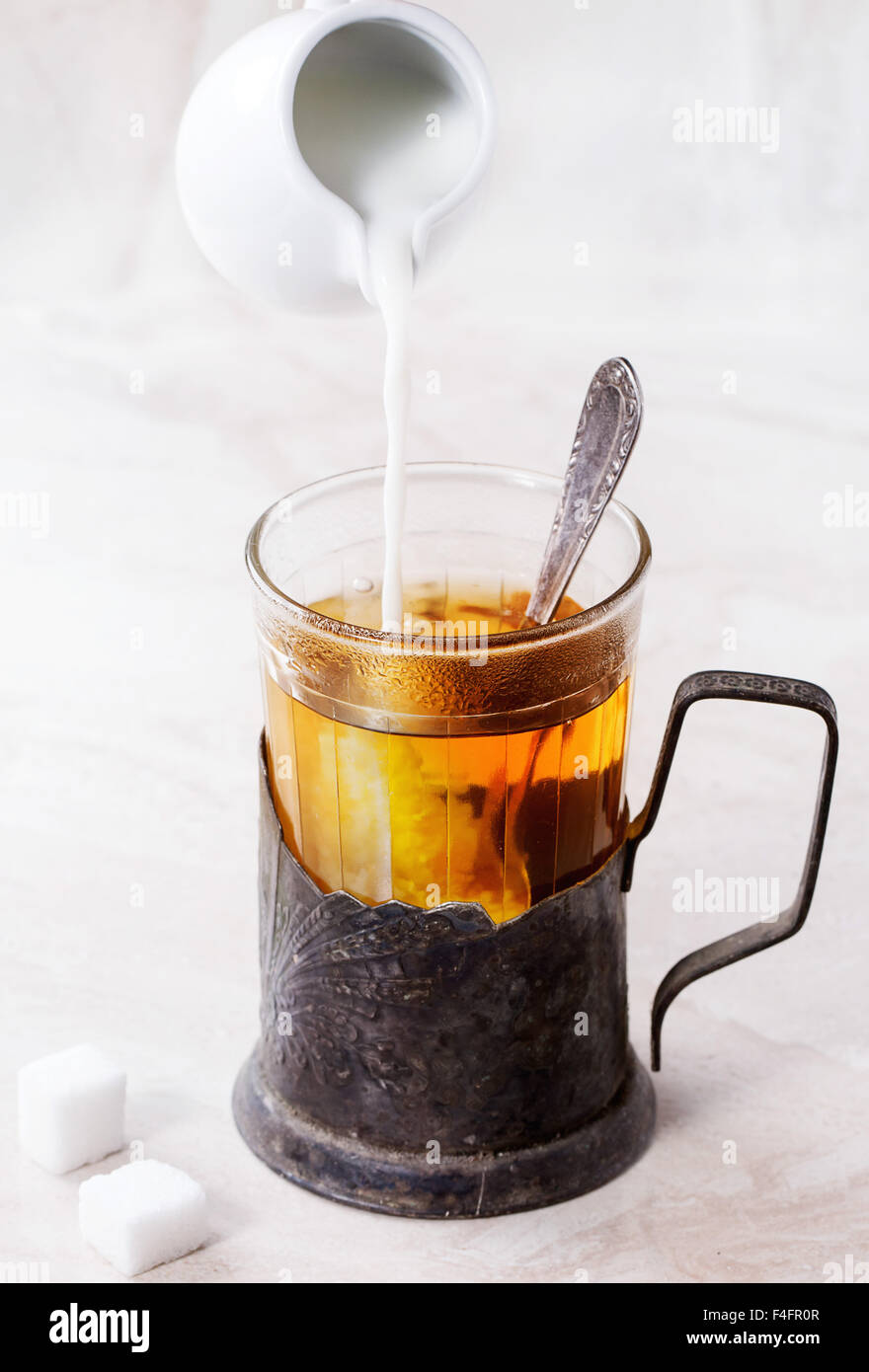 Versare il latte dalla caraffa del bianco al retrò tazza di tè caldo in vetro vintage-titolare con cucchiaino e cubetti di zucchero su marmo bianco bac Foto Stock