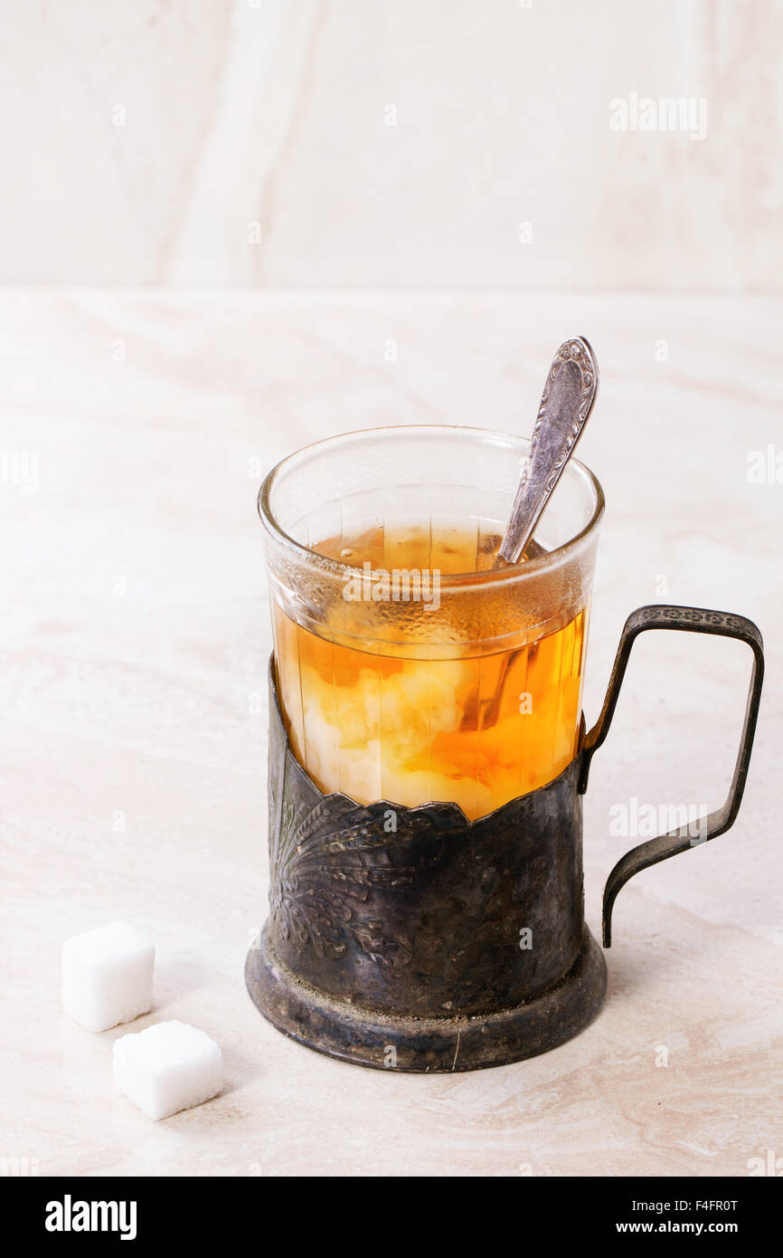 Il latte si scioglie nel retro tazza di tè caldo in vetro vintage-titolare con cucchiaino e cubetti di zucchero su marmo bianco backgtound. Foto Stock