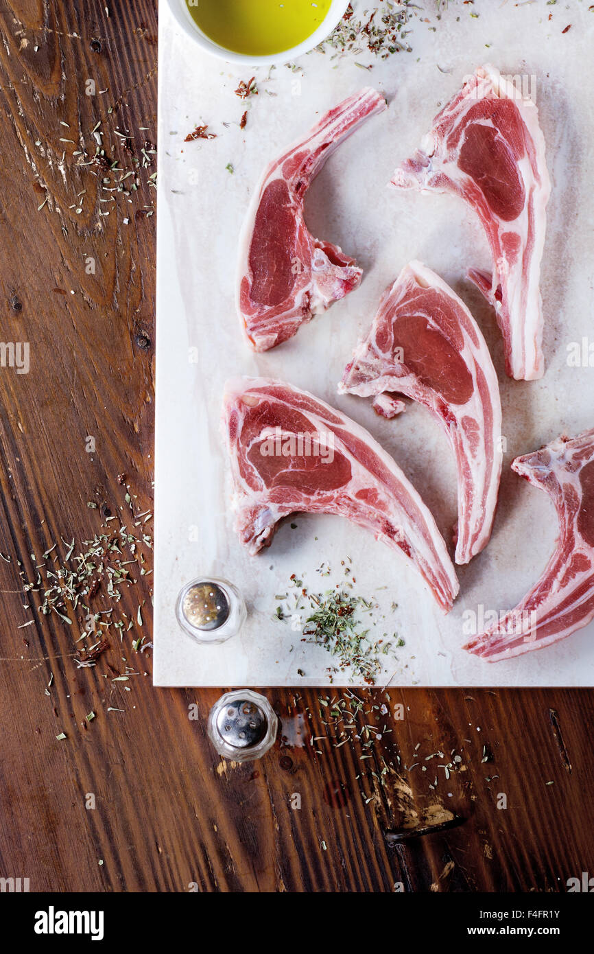 Materie costolette di agnello con sale e pepe, asciugare le erbe aromatiche e la coppa dell' olio d' oliva sul marmo scheda sopra un tavolo di legno. Vista dall'alto. Foto Stock