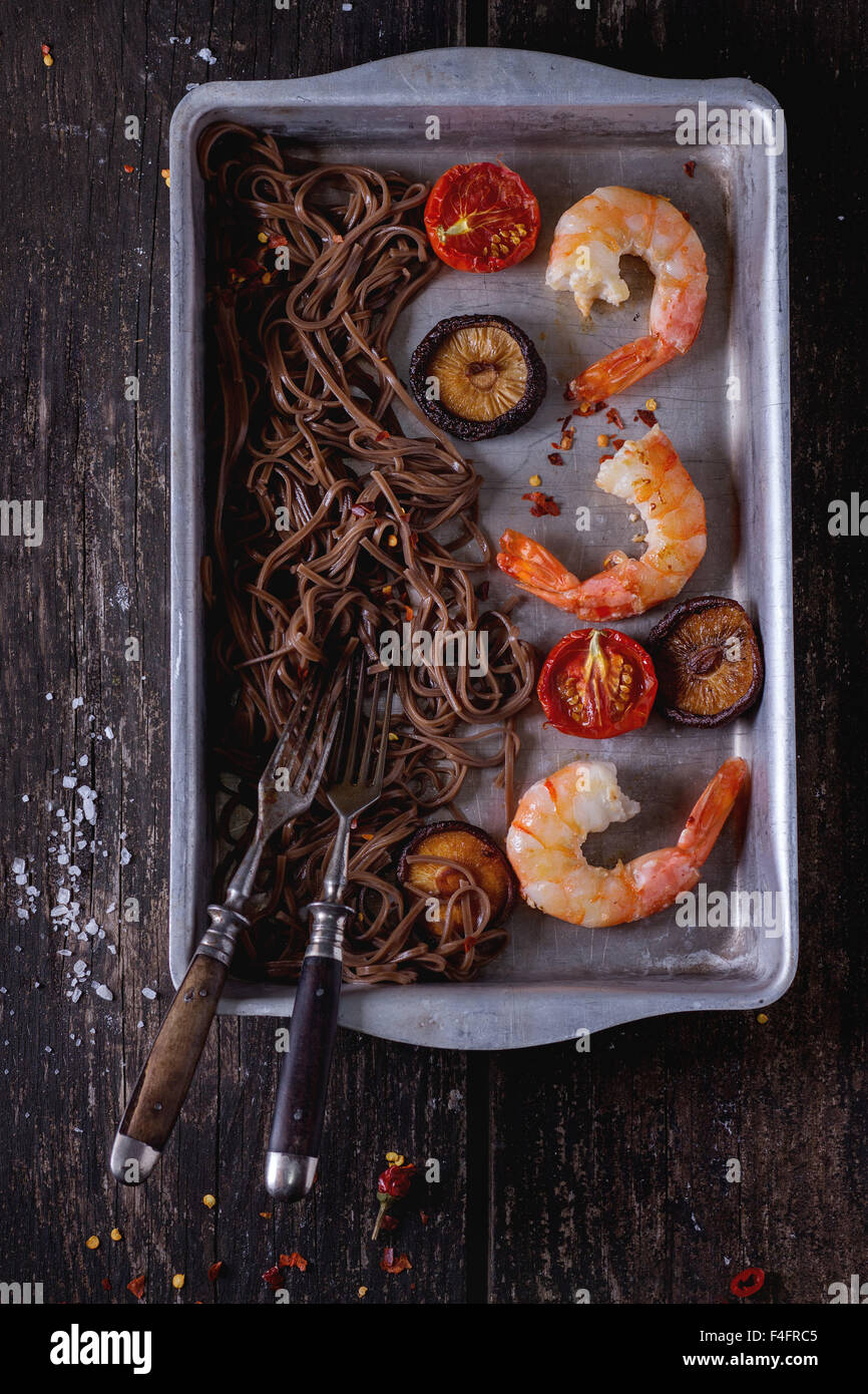 Stile asiatico la cena con la sua pasta di soba, funghi shiitake, grigliate di pomodori e gamberetti in alluminio teglia con forcella vintage Foto Stock