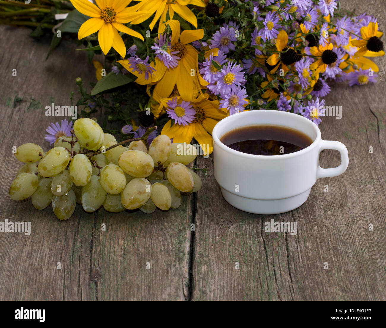Grappolo di uva, caffè e bouquet di fiori selvatici su una tavola di legno, una vita ancora Foto Stock