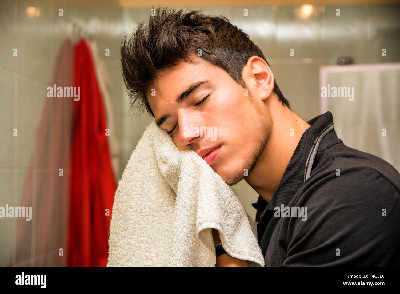 Giovane uomo faccia di essiccazione con asciugamano come parte della quotidiana routine di igiene Foto Stock