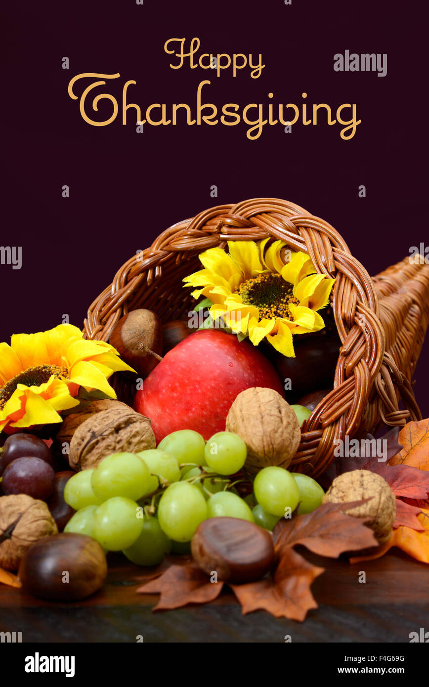 Ringraziamento cornucopia, vimini corno dell'abbondanza, centrotavola con frutta, foglie e girasoli su legno scuro tavolo. Foto Stock