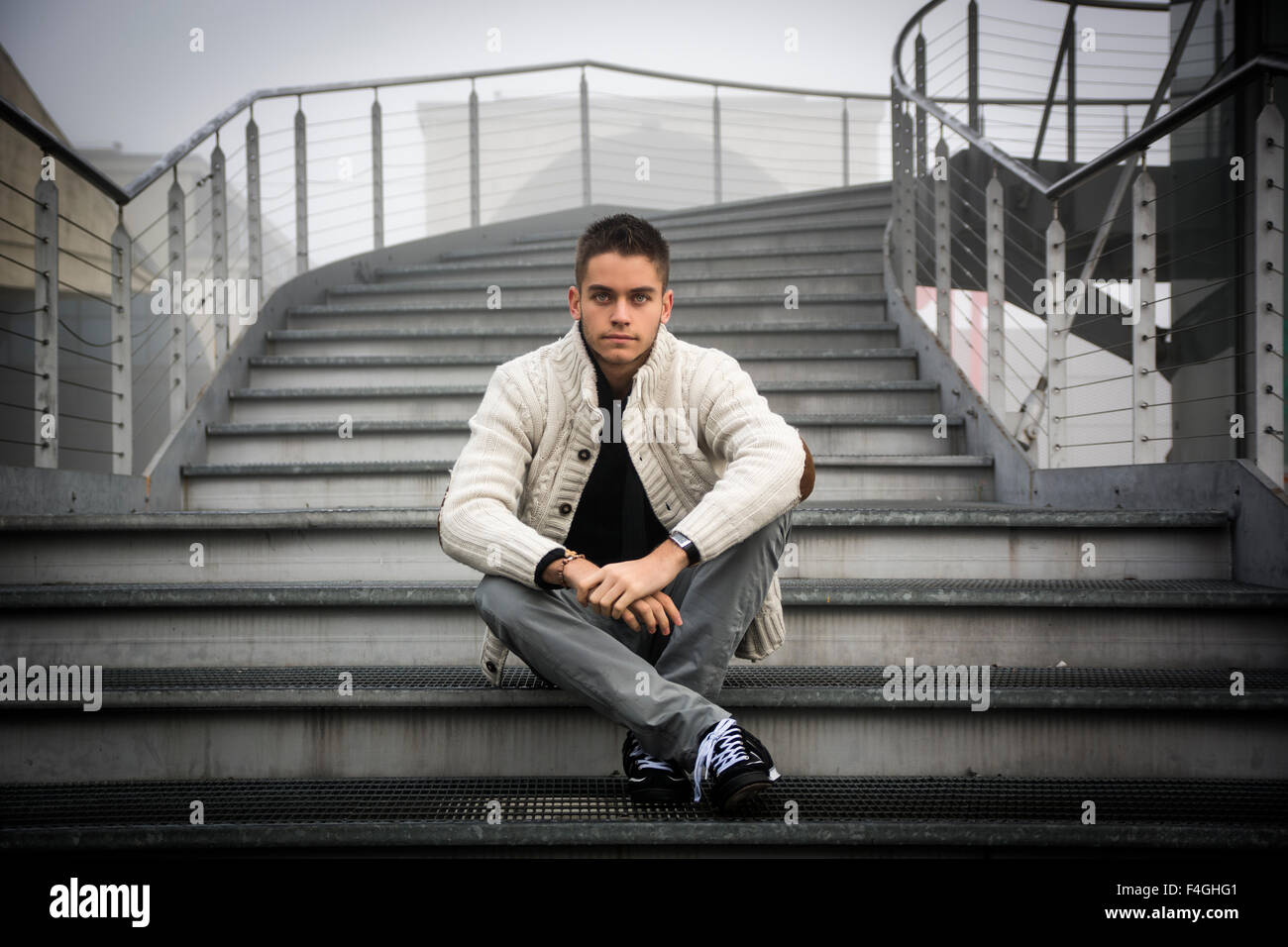 Ben vestito bel giovane in abiti casual seduta zampe trasversale sulla parte inferiore di una scalinata esterna in inverno Foto Stock