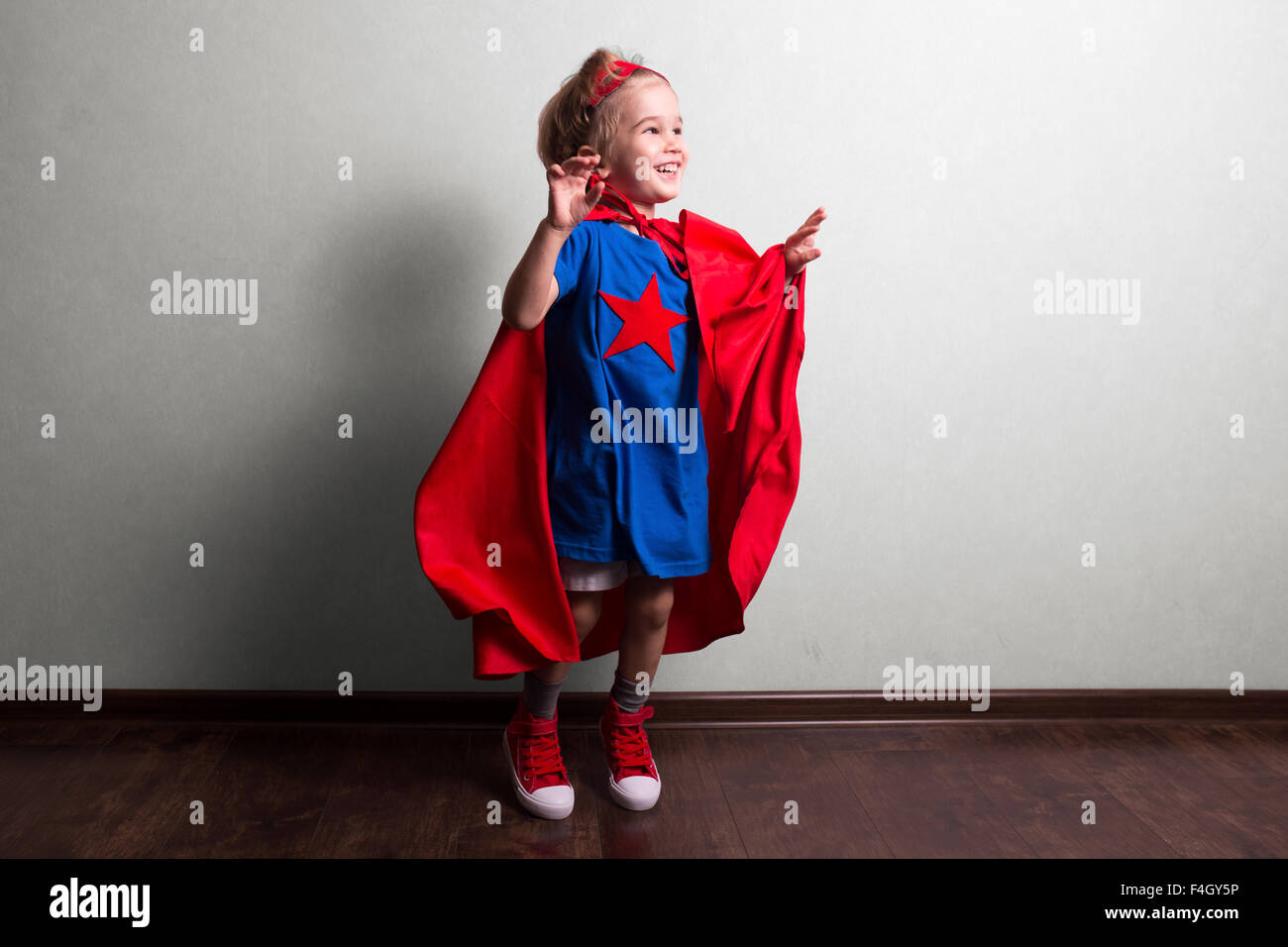 Bambino felice in tuta del supereroe contro il muro grigio. Foto Stock