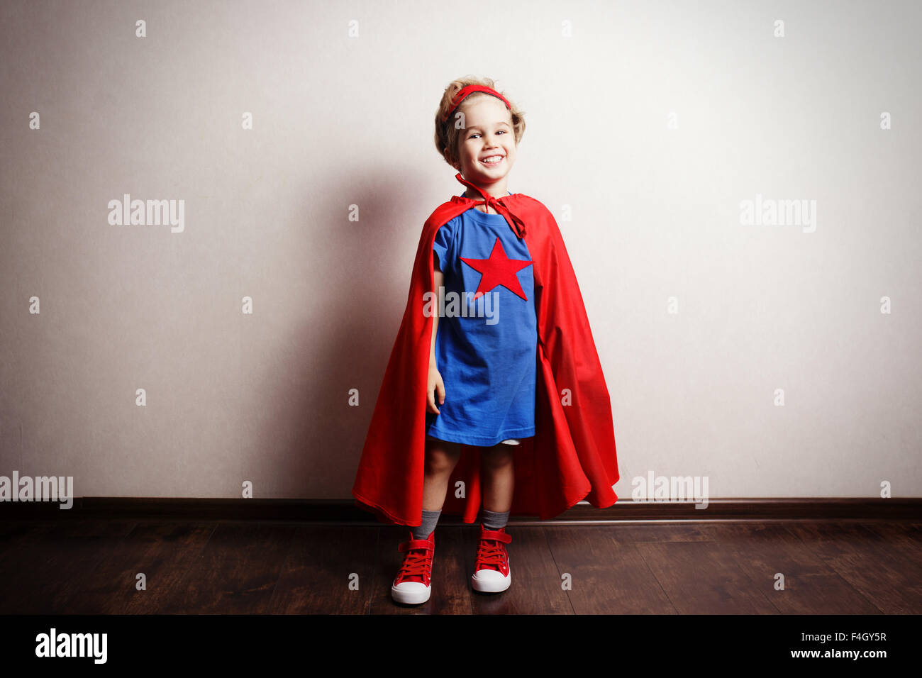 Bambino felice in tuta del supereroe contro il muro grigio. Foto Stock