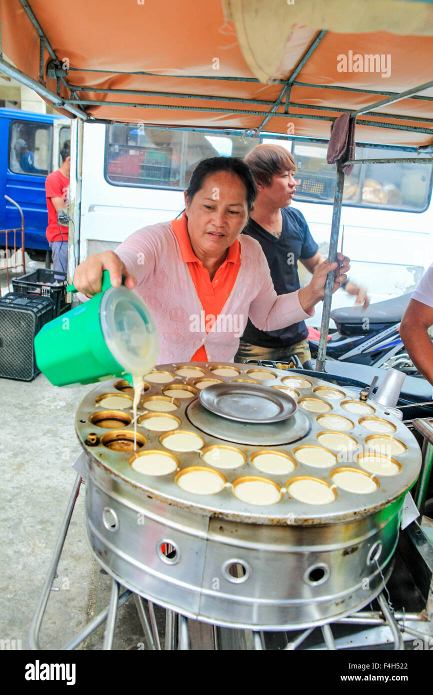 Una donna street food venditore versa la pastella in coppette individuali sul suo biscotto macchina di cottura. Foto Stock