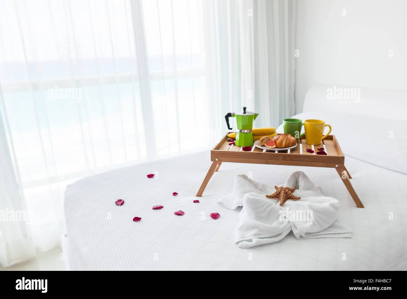 Colazione vassoio in legno con caffettiera e croissant sul letto, decorate starfish su asciugamano bianco Foto Stock