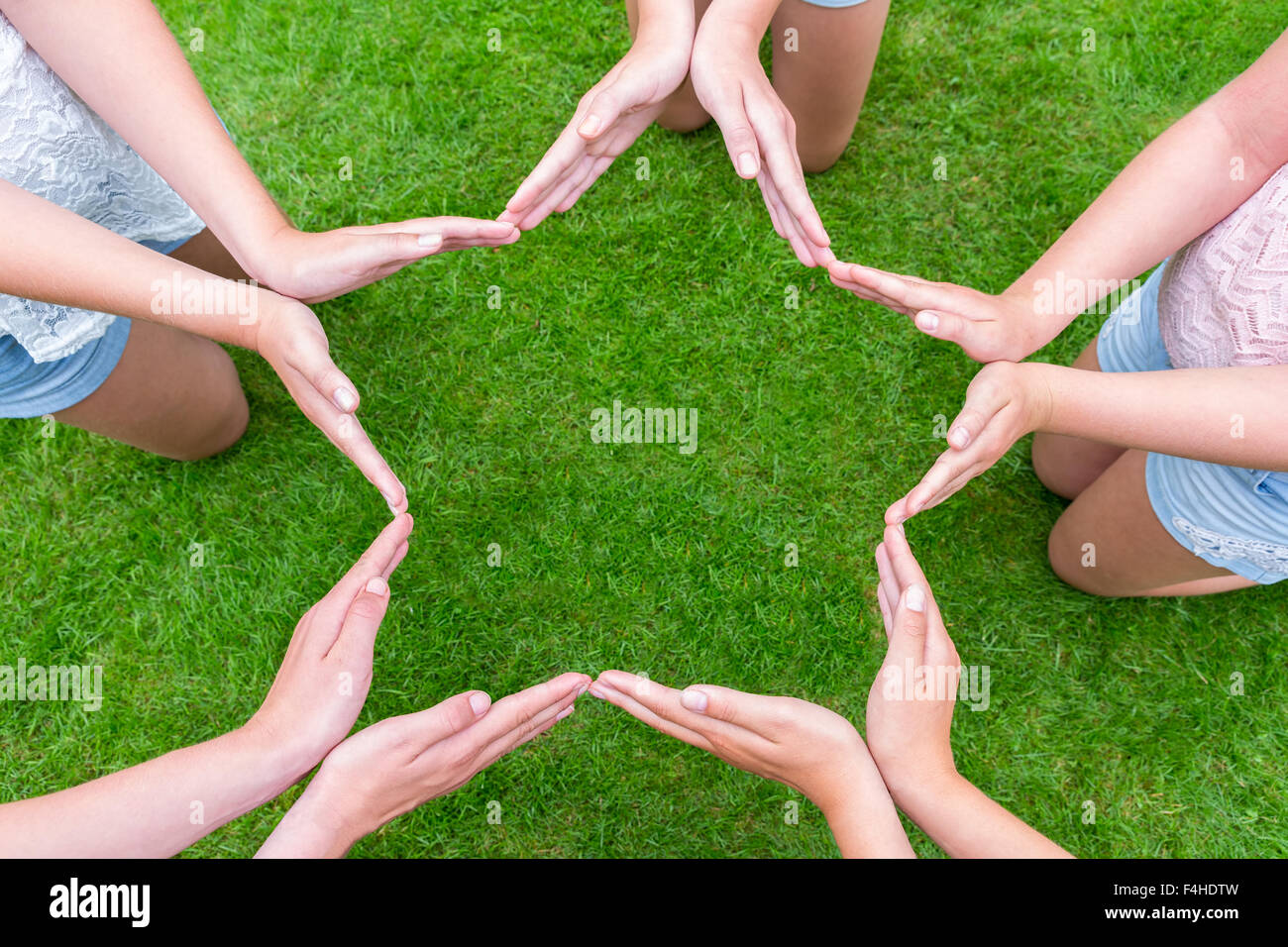 Bracci di bambini con le mani rendendo forma a stella al di sopra di erba verde Foto Stock