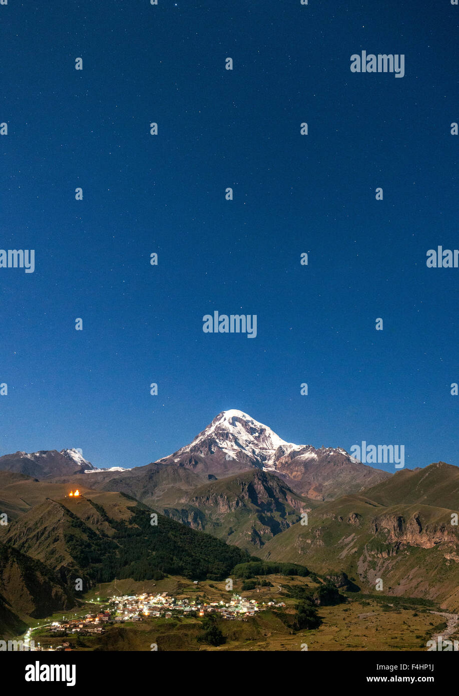 Moonlit vista del monte Kazbek (5047 m), il villaggio di Gergeti e Gergeti Trinity Church nelle montagne del Caucaso della Georgia. Foto Stock