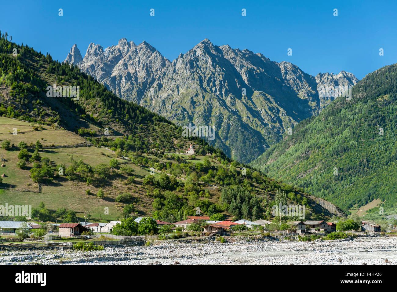 Chiesa nelle colline ai piedi delle montagne che circondano il villaggio di Mestia nella regione di Svaneti del nord ovest della Georgia. Foto Stock