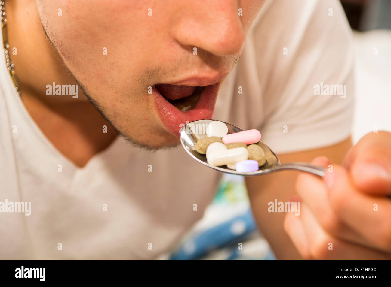 Attraente giovane uomo nel letto di mangiare un cucchiaio colmo di medicina, compresse e pillole Foto Stock