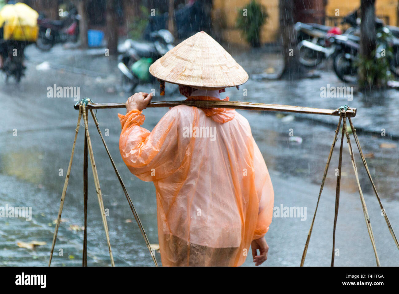 Signora vietnamita in plastica con il mac su porta il suo giogo con frutto per la vendita attraverso le strade di Hoi An, Vietnam centrale,Asia Foto Stock