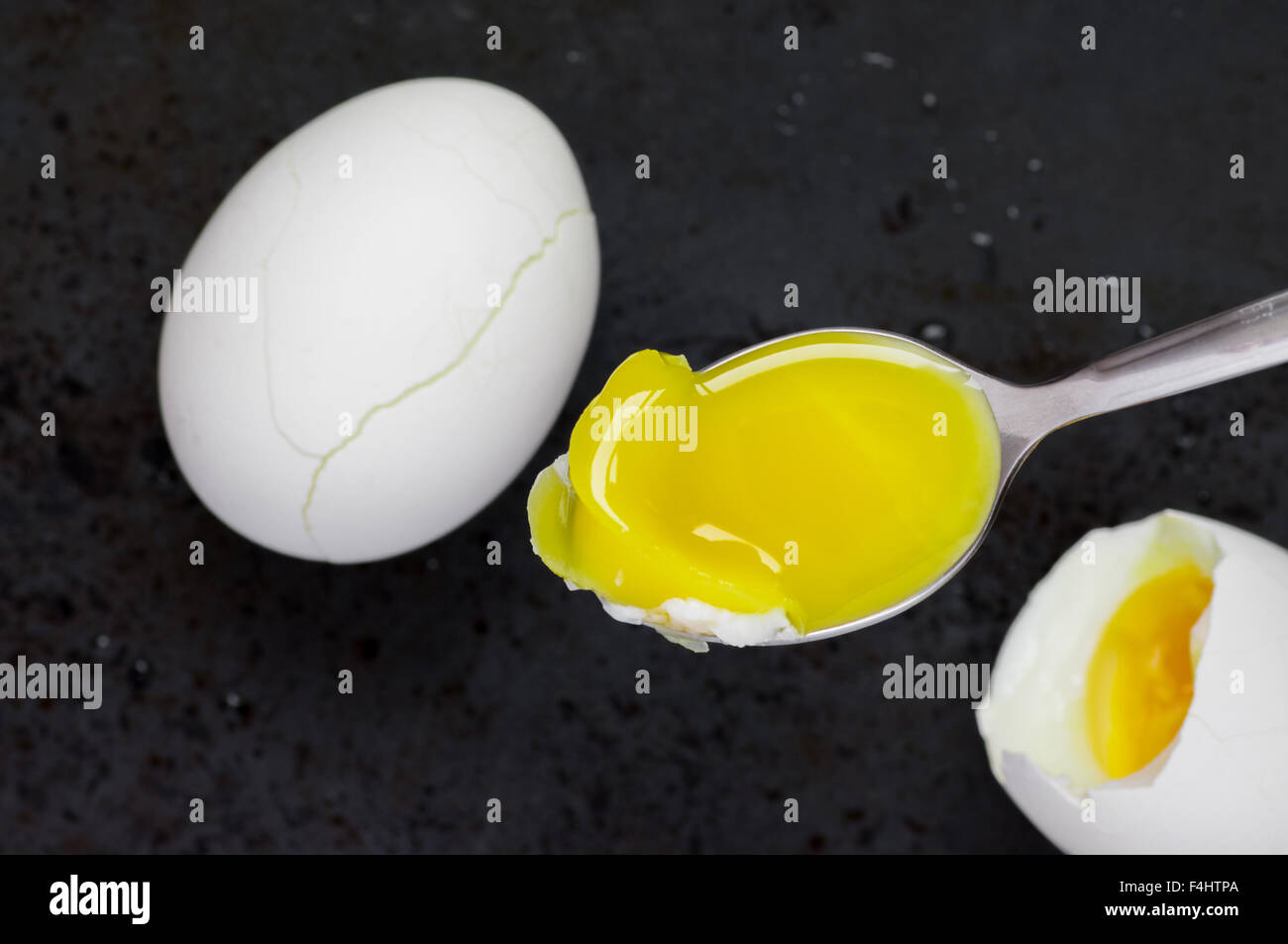 Cucchiaio con tuorlo d'uovo sodo su uno sfondo nero in vista superiore Foto Stock