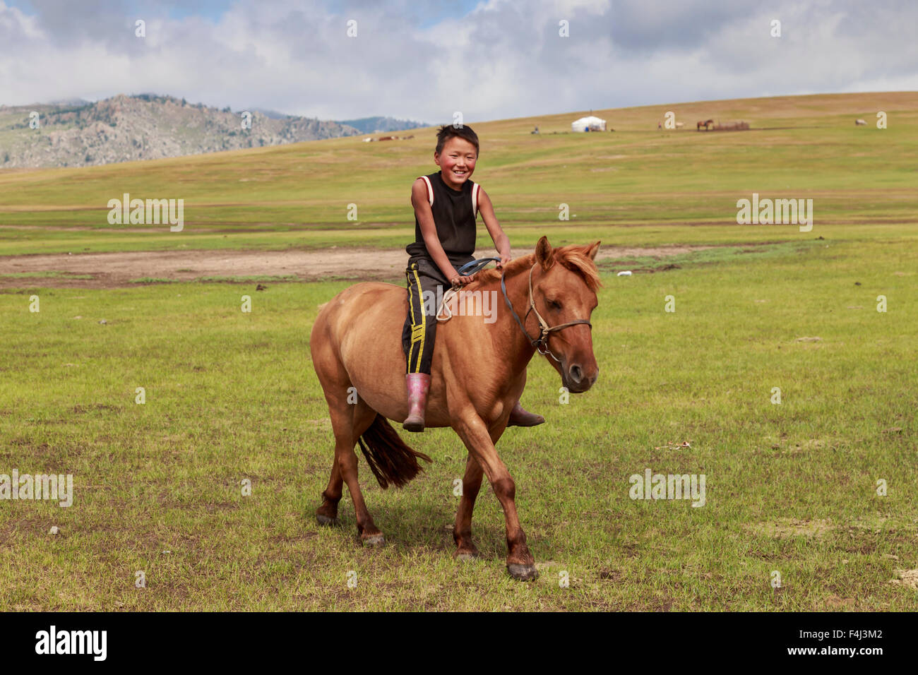 Cavallo e sorridente boy riding bareback con ger e colline dietro ad estate campo nomadi, Khujirt, Uvurkhangai, Mongolia centrale Foto Stock