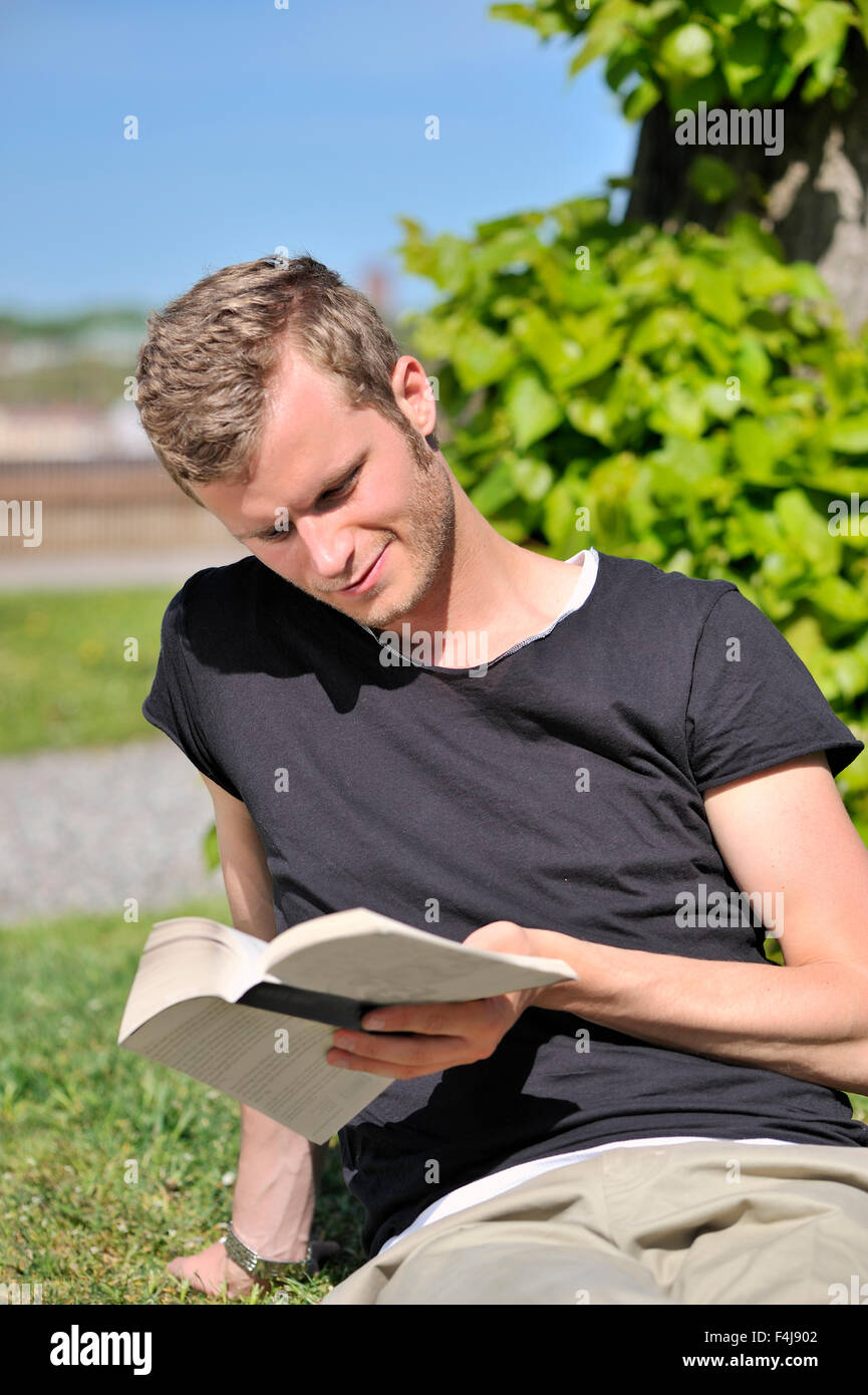 Giovane uomo di lettura da un albero, Svezia. Foto Stock