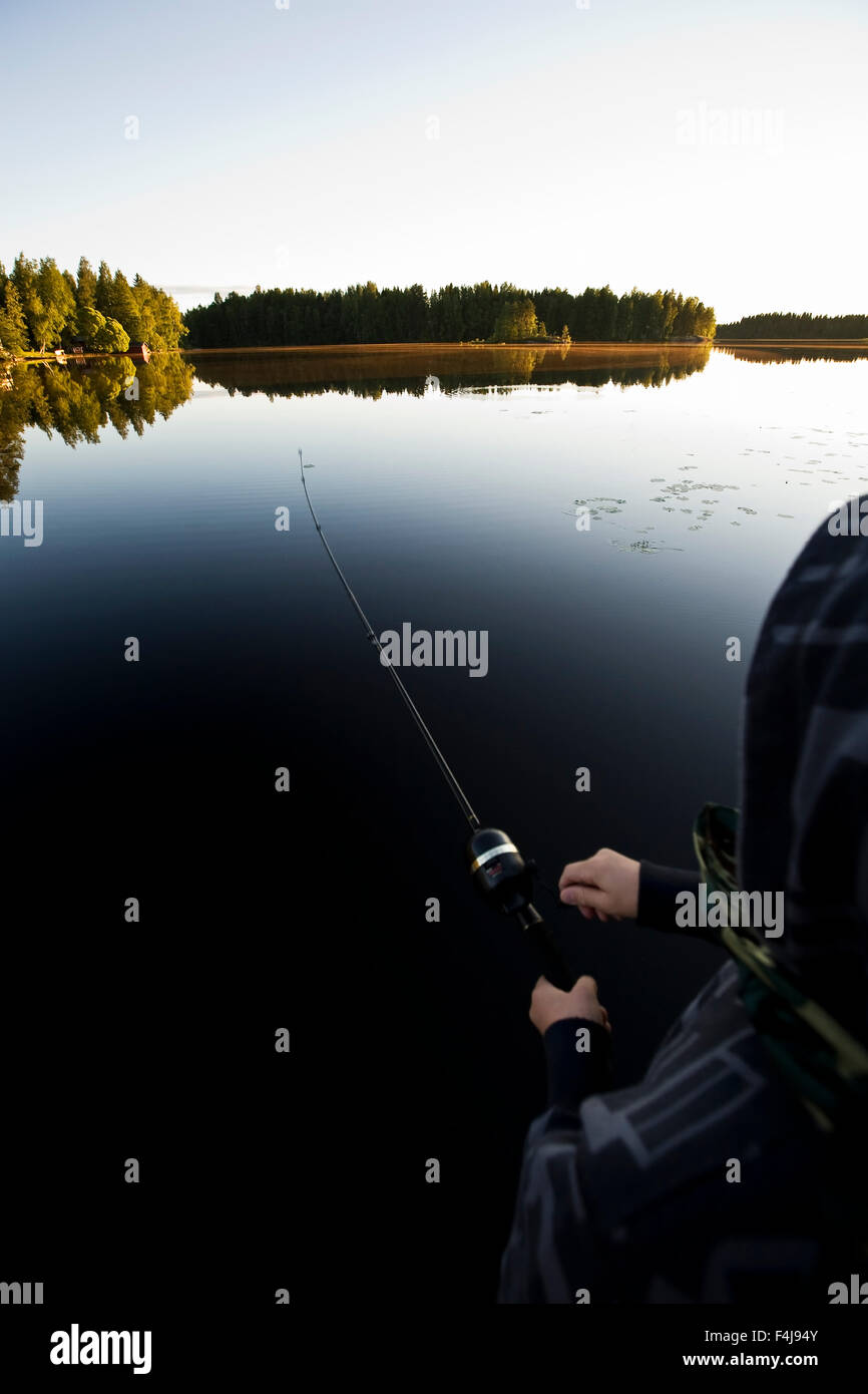 Ragazzo di pesca in un lago calmo al tramonto, Finlandia. Foto Stock