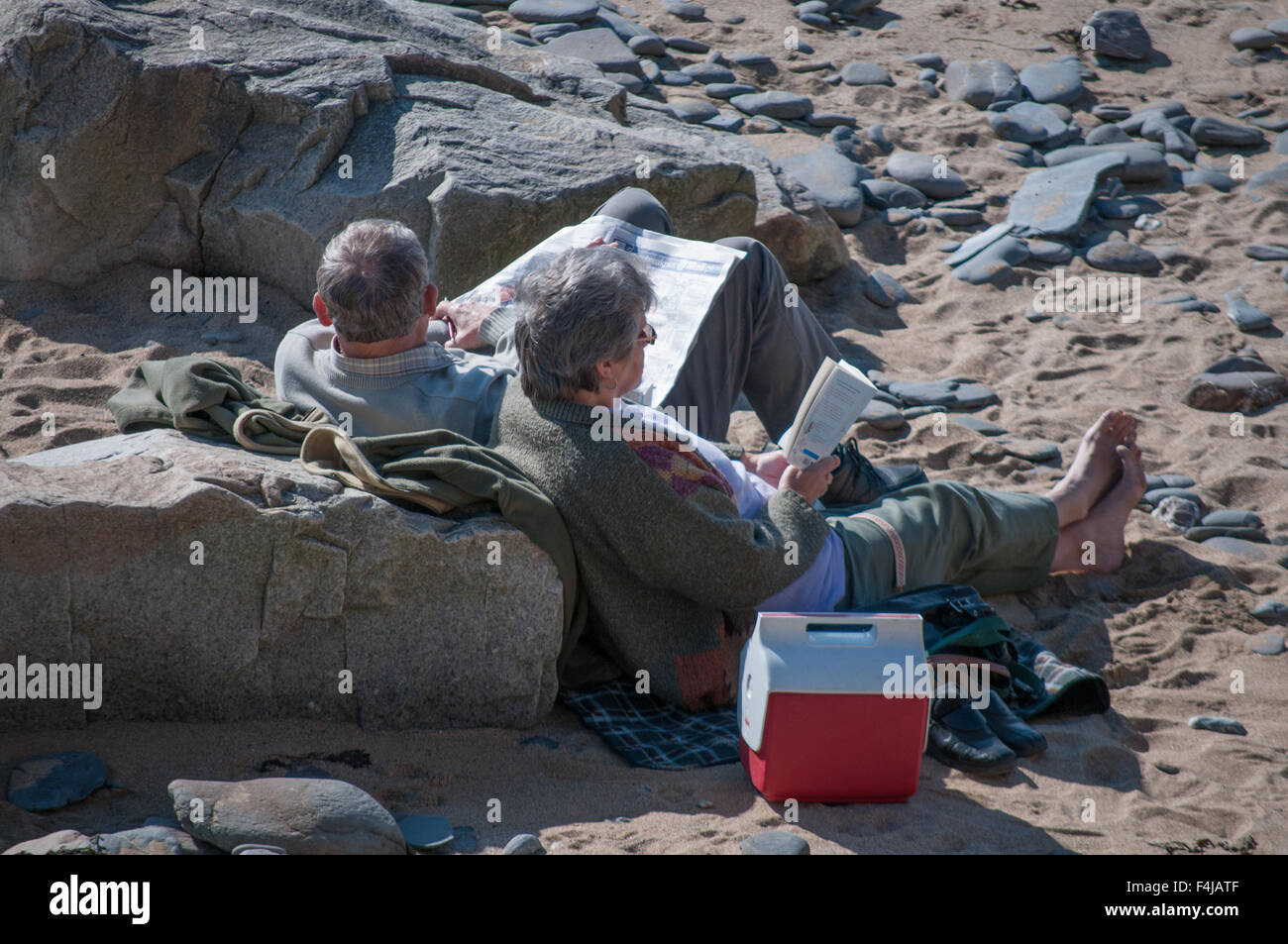 Un paio di loro 60's lettura su una spiaggia in Cornovaglia Foto Stock