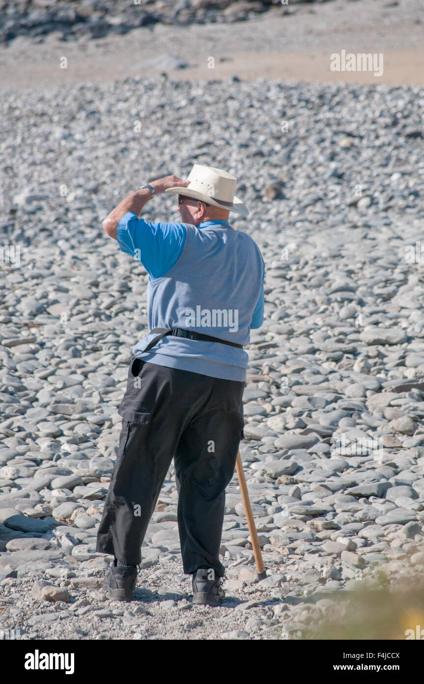 Un uomo tiene un bastone da passeggio mentre guardando attraverso una spiaggia in Cornwall, Regno Unito Foto Stock