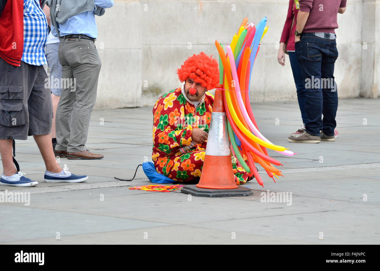 Londra, Inghilterra, Regno Unito. Clown con palloncini seduto in Trafalgar Square Foto Stock