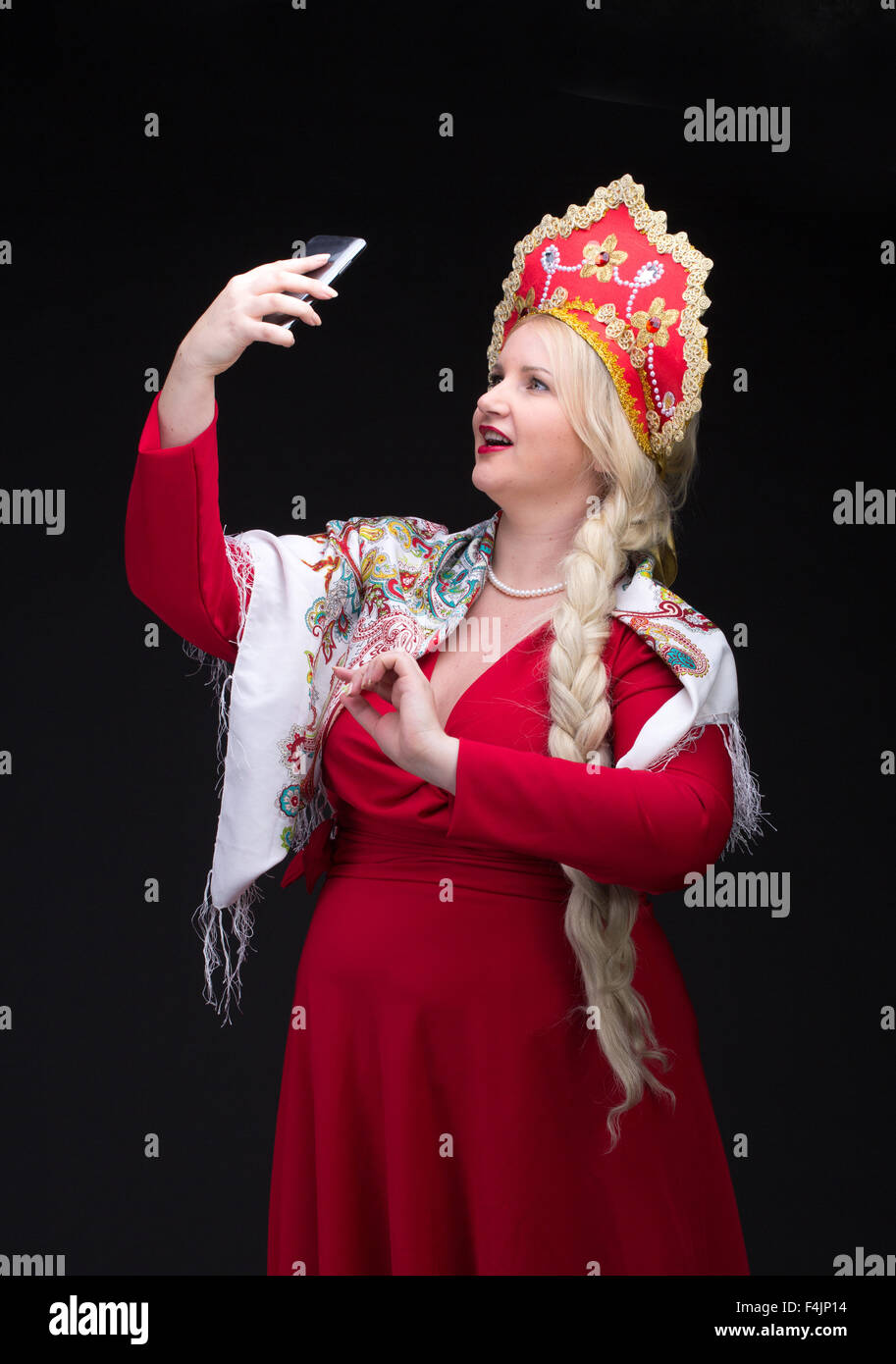 Ragazza in piedi in russo in costume tradizionale. Fare selfie. La donna indossa sarafan e kokoshnik. La ragazza in rosso il vecchio russo dre Foto Stock