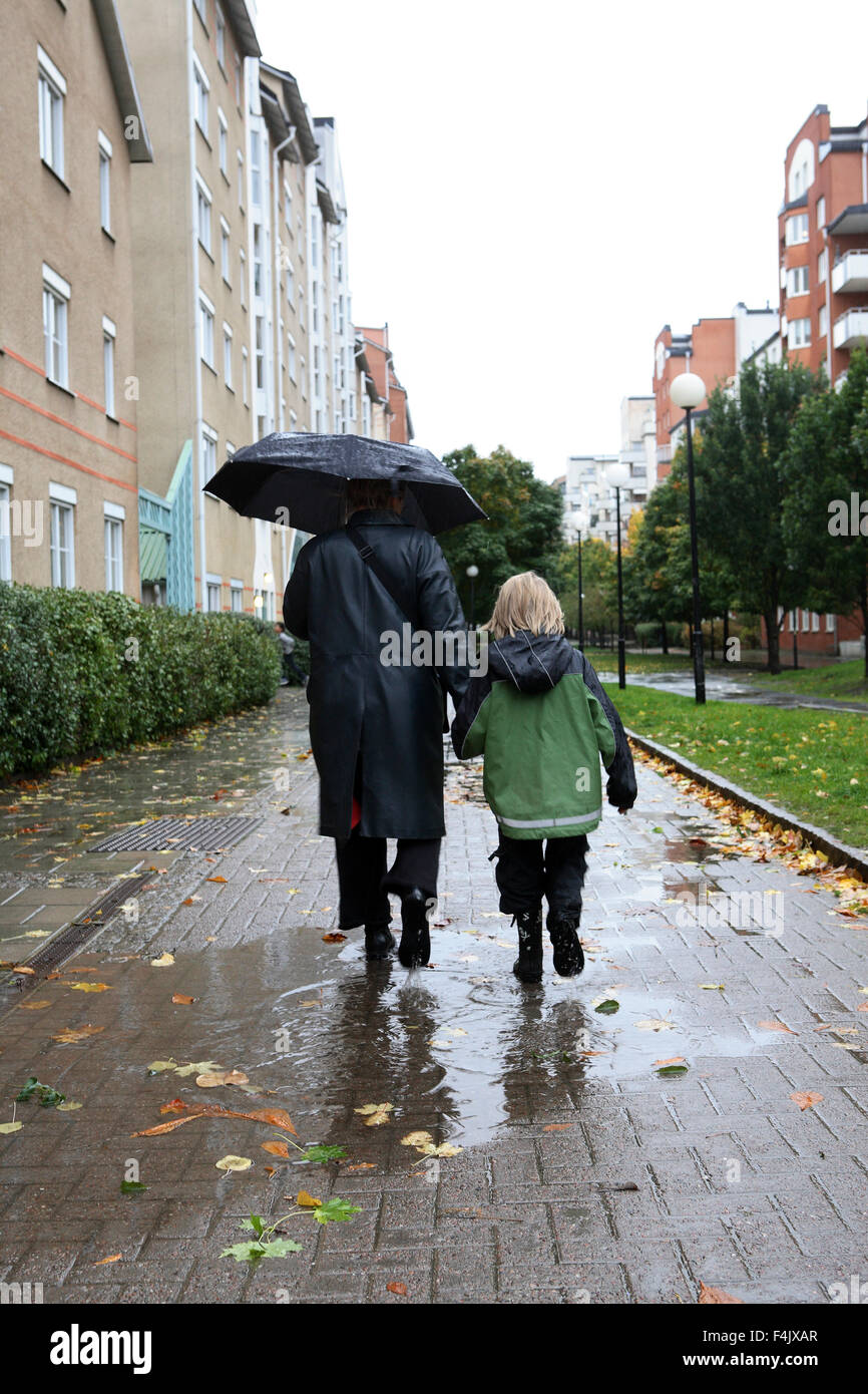 La madre e il figlio a piedi attraverso il marciapiede durante la pioggia Foto Stock