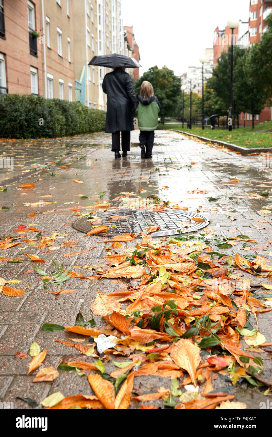La madre e il figlio a piedi attraverso il marciapiede durante la pioggia Foto Stock