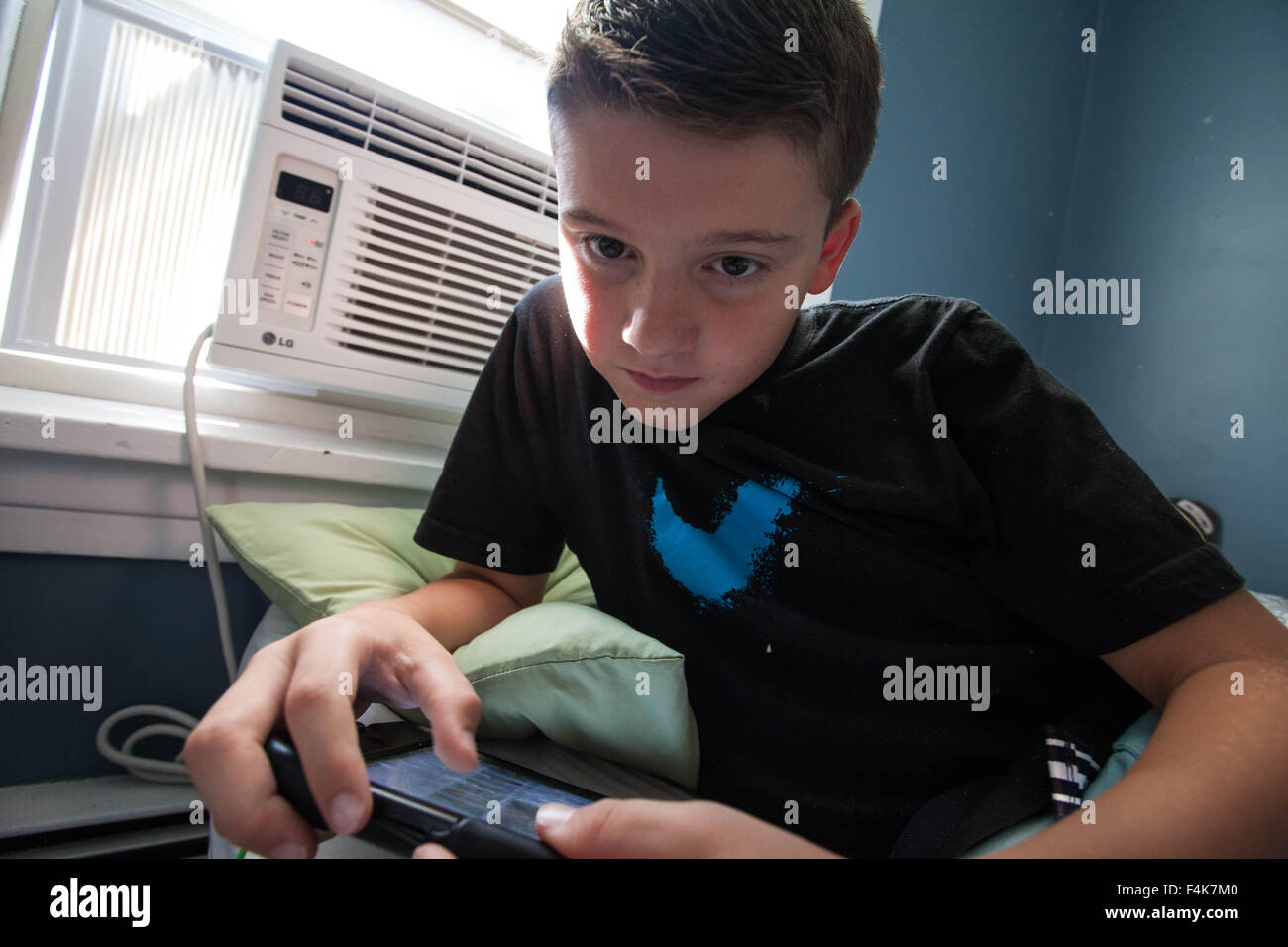 Un giovane ragazzo guarda al suo tablet da sola nella sua camera da letto in una giornata di sole Foto Stock