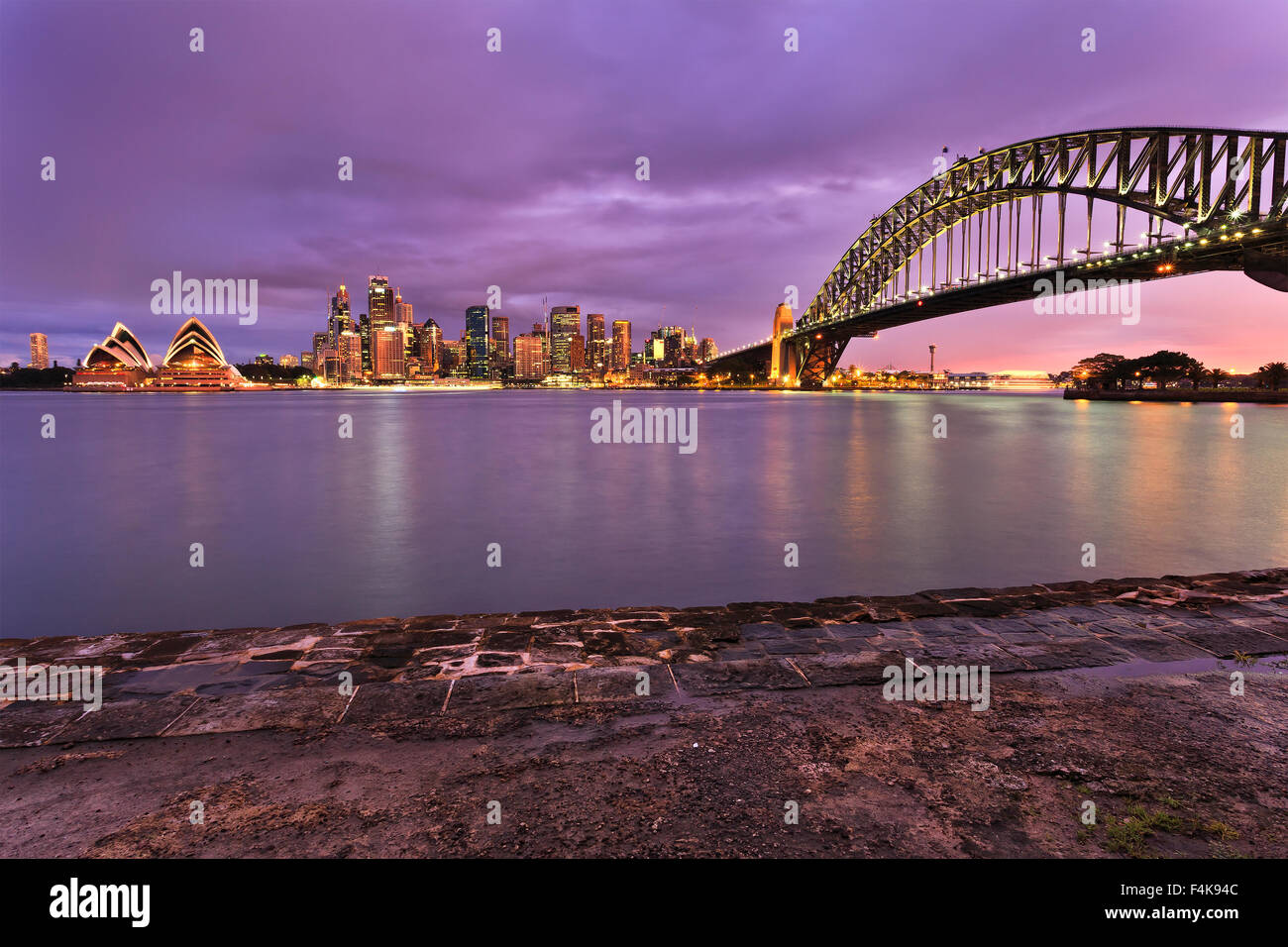 La città di Sydney CBD monumenti illuminati al tramonto e visualizzati attraverso il porto da Milsons Point. Il Sydney Harbour Bridge, grattacieli Foto Stock