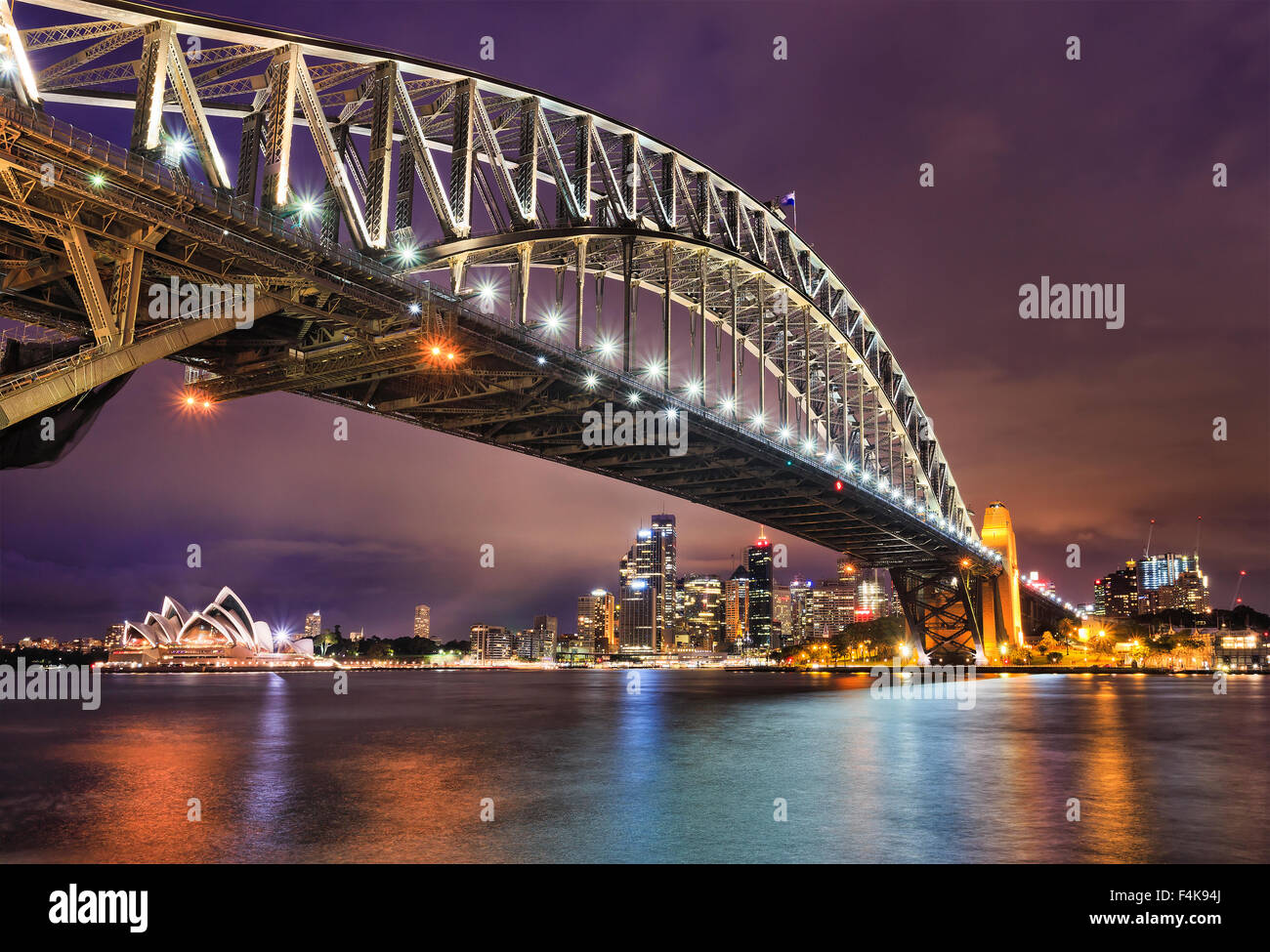Sul lato est del Ponte del Porto di Sydney al Tramonto con illuminazione brillante di arco in acciaio e colonne riflettendo in acque sfocata Foto Stock