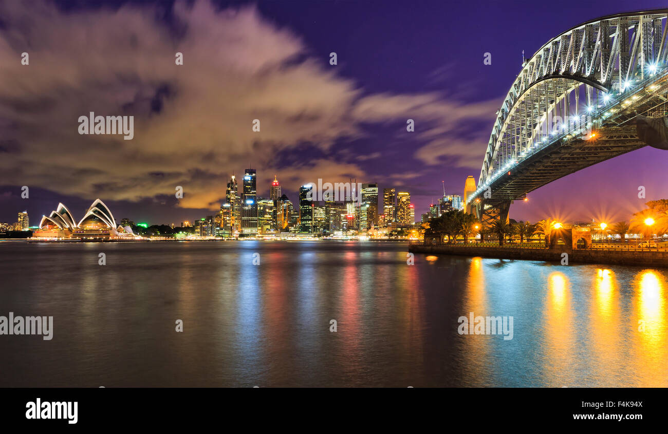 Australia Sydney CBD cityline attraverso harbour con sky-raschiatori, opera e Harbour Bridge al tramonto è completamente illuminata Foto Stock