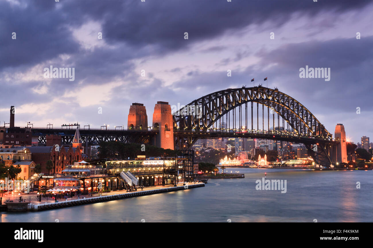 Il Ponte del Porto di Sydney - Vista laterale dal Circular Quay al tramonto sotto le nuvole pesanti altamente illuminato Foto Stock