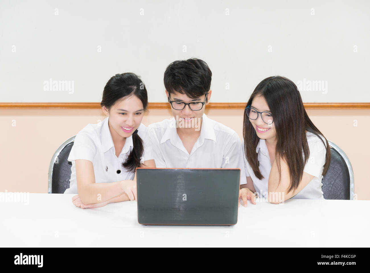 Un gruppo di studenti asiatici in uniforme e-learning attraverso il computer portatile in aula Foto Stock